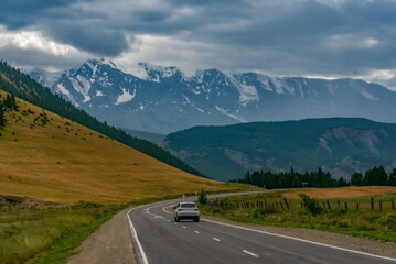 Asphalt highway with a moving car leading to the mountains in the Altai Mountains