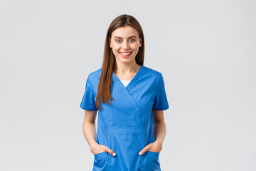 Healthcare workers, prevent virus, insurance and medicine concept. Cheerful smiling beautiful doctor, female nurse in blue scrubs, intern in hospital staying positive, standing grey background