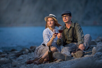 a young man and a woman drink red wine on the beach from glasses, sitting on a blanket in the evening. Night Portrait