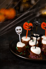 Sweet Halloween treat, chocolate covered marshmallows with sugar and Halloween decorations on a black plate, vertical photo with soft focus