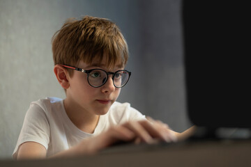 Boy in glasses enthusiastically plays computer games. Teen boy is studying online. Preparing to exams