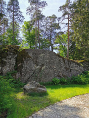 A boulder fence next to a path paved with cobblestones in the rocky natural park Monrepos of the city of Vyborg on a clear summer day.