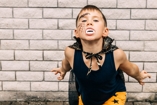 Portrait of boy in vampire halloween costume with painted face showing fangs at camera in park. Copy space