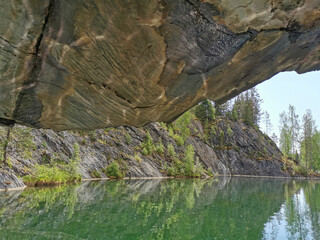 View from the grotto with a textured ceiling and reflections from the water on the steep slope of the flooded Marble Canyon in the mountain park Ruskeala.