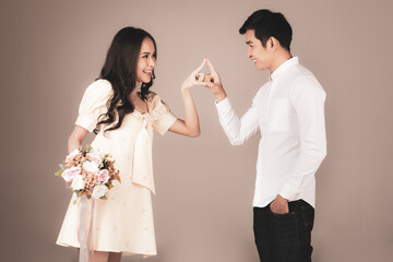 Portrait of young attractive Asian couple, man wearing white shirt, woman wearing beige dress standing together playing, woman holding bouquet of flower. Concept for pre wedding photography