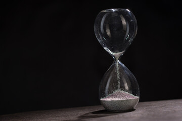 An hourglass in which the last grains of sand fall on a dark background with a bokeh effect