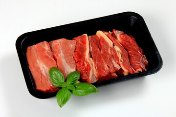 Raw beef meat in a black plastic container. Opened black plastic tray with raw cut meat