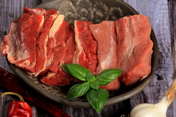 Raw beef bones in round clay bowl on wooden table decorated with vegetables and spices, vintage hunter knife. Beef selection for broth