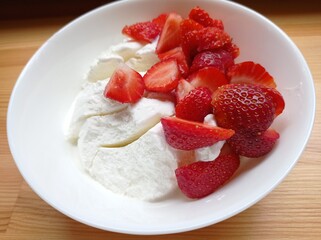 Ice cream and strawberry slices. Delicious summer dessert in a white plate on a wooden countertop
