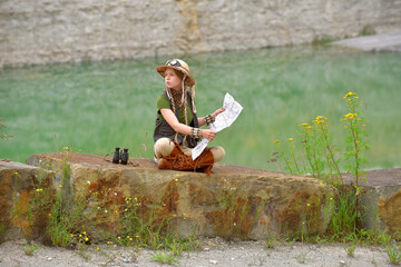 A young girl is dressed up as an explorer. She 
is seen sitting on a large boulder in a...