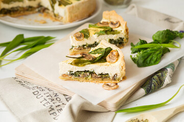 French cuisine. Quiche with mushrooms, spinach and wild leeks. Green food. French pastries on a white table. Pie with cheese and mushrooms, wild garlic. French dish with spinach, wild garlic.