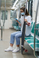 Millennial girl passenger using mobile phone wear disposable mask against coronavirus in subway...