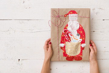 Top view of a beautifully wrapped handmade gift. The girl holds a gift with a hand-made article in...