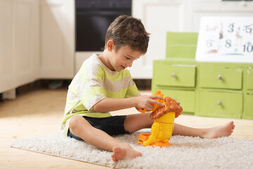 A boy of 7 years old seats on the carpet and plays with toys at home. Educational games for children