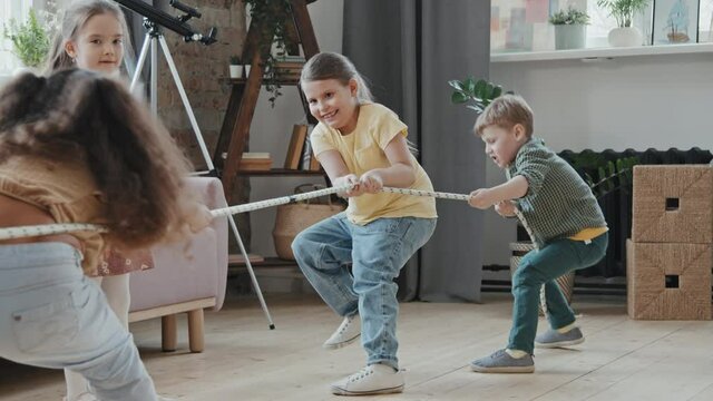 Slowmo shot of cute little boys and girls pulling rope and playing tug of war in living room at home