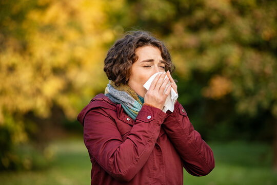 Woman in park sneezing and blowing nose