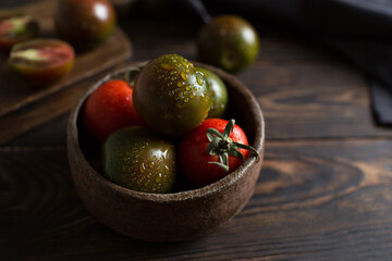 A fresh crop of black tomatoes. Macro photography of tomatoes. Kumato variety on a brown wooden background. Vegetables in a ceramic plate. Dark photos of vegetables. Water droplets on a tomato. Raw 