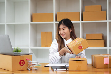 Plakat Startup small business entrepreneur SME, young asian woman working with laptop computer and delivery packaging box, online market packing, SME e-commerce seller concept.