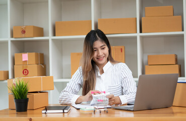 Startup small business entrepreneur SME, young asian woman working with laptop computer and delivery packaging box, online market packing, SME e-commerce seller concept.