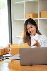 Startup small business entrepreneur SME, young asian woman working with laptop computer and delivery packaging box, online market packing, SME e-commerce seller concept.