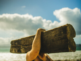 man carrying old wooden log by the beach