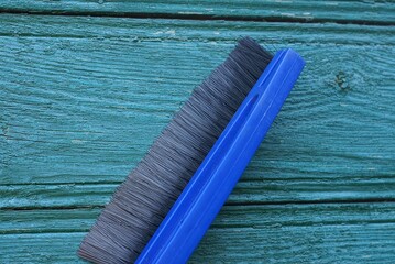 a blue plastic brush with black bristles sweeps away dust and dirt on a green wooden wall