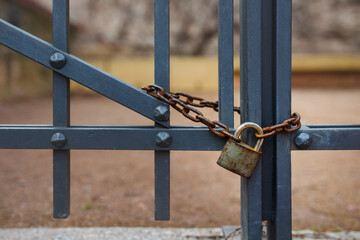 Detail of a metal gate locked with a rusty padlock and chain.