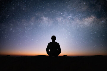Silhouette of young traveler sitting and meditating with the star and milky way alone on top of the mountain. He enjoyed traveling and was successful when he reached the summit. - obrazy, fototapety, plakaty