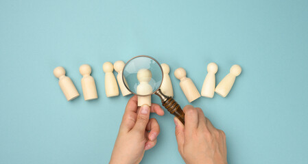 wooden men and a magnifying glass on a blue background. Recruitment concept, search for talented and capable employees, career growth - obrazy, fototapety, plakaty