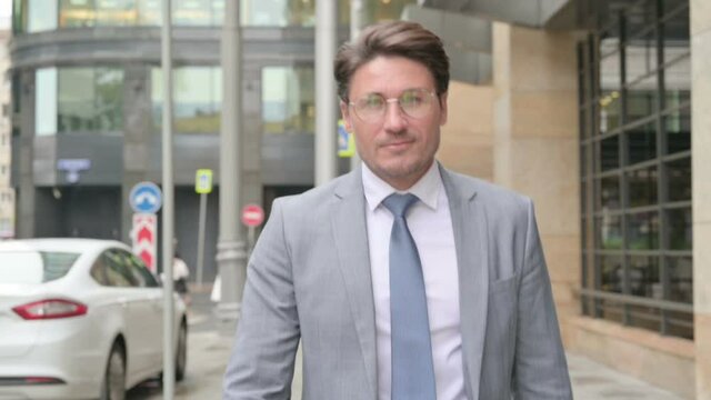 Middle Aged Businessman Walking Towards Camera In Street 