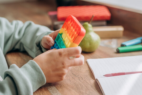 Close-up of schoolgirl playing with colorful pop-it fidget toy while studying at home.Trendy anxiety and stress relief fidgeting game.School concept.