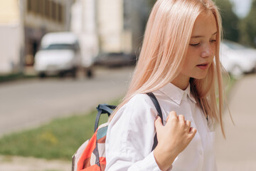 Fototapeta premium Serious blonde teenage girl in a school uniform and a backpack is walking down the street to school.Back to school concept.Copy space for text.