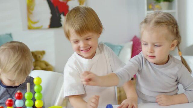 Excited little boys and girl making toy block tower come crashing down and smiling while playing together in kindergarten