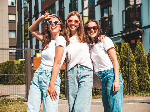 Three young beautiful smiling hipster female in trendy summer same clothes. Sexy carefree women posing on the street background.Positive models having fun in sunglasses.Hugging. Cheerful and happy