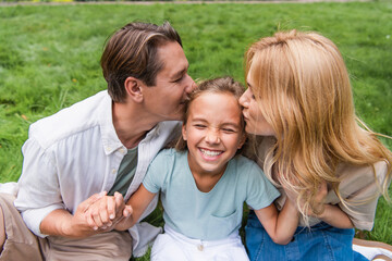 Fototapeta premium Parents kissing daughter on lawn