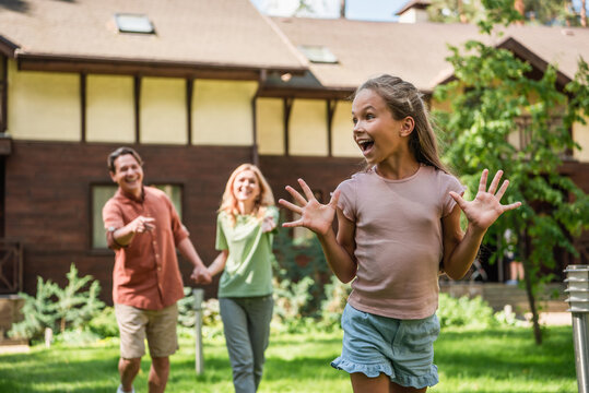 Positive kid standing near parents and blurred vacation house