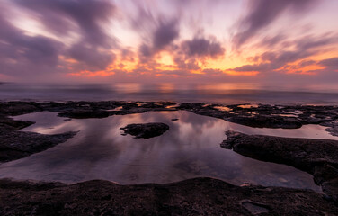 amazing scenic view at a sea shore from a coast after dramatic colorful sunset with flying blured clouds and reflection on water surface , beautiful ocean landscape