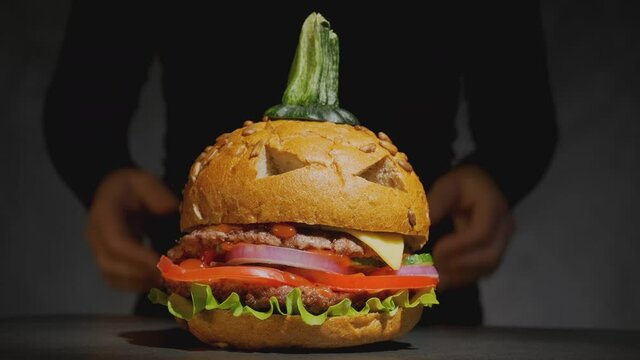Female hands of waiter serve beef burger in image of pumpkin for Halloween on black background. halloween party dish.