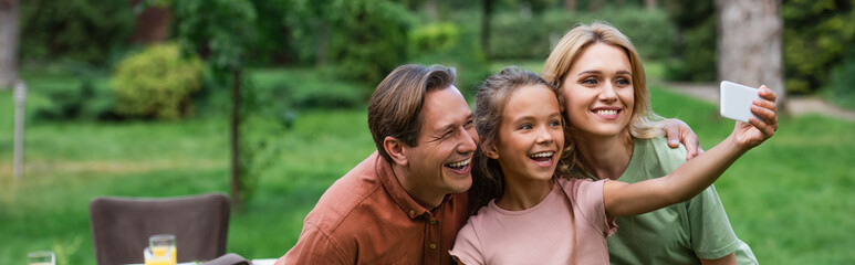 Obraz premium Smiling girl talking selfie with parents outdoors, banner