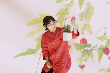 붉은색 옷을 입은 한국의 평범한  50대 주부가 작은 꽃이 핀 꽃 바구니를 들고 있는 모습입니다.  - obrazy, fototapety, plakaty
