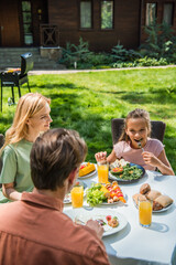 Kid eating salad and looking at father during picnic outdoors
