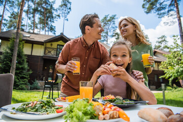 Positive kid looking at camera near food and parents outdoors