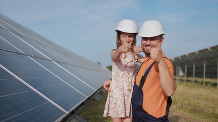 A father, a solar power engineer, and his daughter are standing near solar panels. The father...