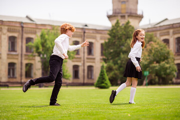 Photo of two people redhead kids play game tag boy try catch sister wear white shirt uniform park outside