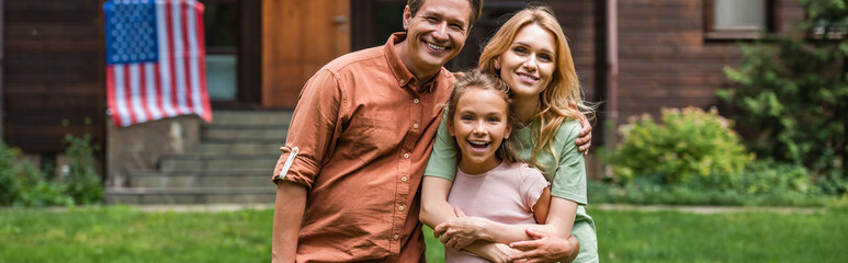 Happy family smiling at camera near blurred american flag outdoors, banner