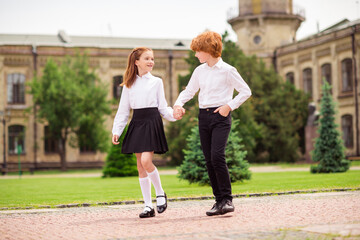 Photo of two relaxed positive dreamy ginger schoolkids walk enjoy hold hands wear white shirt...
