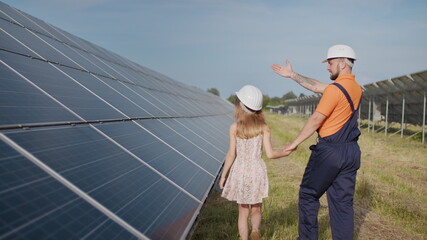 A father working in a solar power plant tells his daughter about his work, shows green energy,...