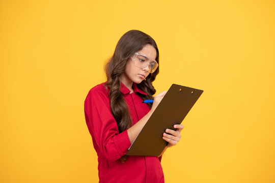 concentrated teenager girl in protective glasses making notes in folder with documents, study