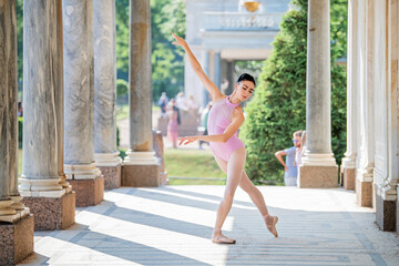 Slender ballerina in pointe shoes and wearing silhouette costume dancing against the background of antique architecture in park