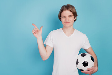 Photo of positive man point finger empty space holding soccer ball isolated blue background